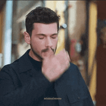 a man with a mustache is smoking a cigarette and covering his mouth with his hand .