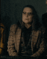 a woman wearing glasses and a plaid jacket is sitting in a dark room