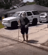 a man with a cane is walking down the sidewalk in front of a white suv .