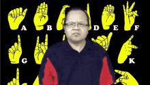 a man wearing glasses stands in front of a sign language alphabet including a b c d e f and k