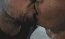 a man with a beard is kissing another man with a white shirt