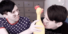 two men with cat faces on their faces are holding a chicken toy .