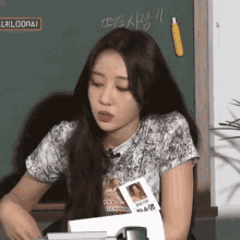 a woman with long hair is sitting in front of a chalkboard with a pencil on it .