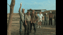 a group of men are standing in a dirt field and one man is holding a bird