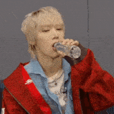 a man in a red jacket is drinking water from a plastic bottle .