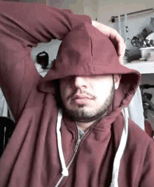a man with a beard is wearing a red hoodie and covering his face .