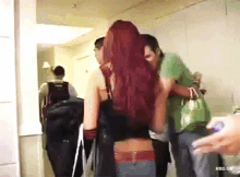 a woman with red hair is walking down a hallway with a man in a green shirt behind her