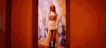 a woman in a white dress is standing in a doorway in a red room .