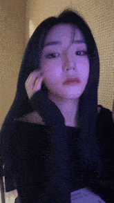 a woman with long black hair is holding her hand to her ear .