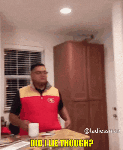 a man in a red and yellow vest is standing in a kitchen and says 