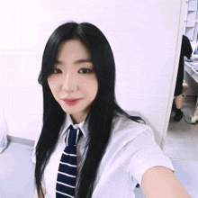 a woman with long black hair is wearing a white shirt and striped tie