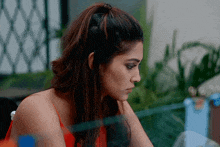 a woman in a red tank top is sitting at a table looking down