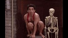 a man is squatting down next to a skeleton .