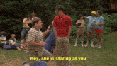 a man in a red shirt is standing in front of a group of people and says " hey she is staring at you "