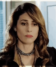 a woman wearing a necklace and earrings is looking at the camera