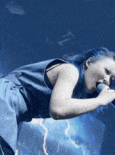 a woman with blue hair is singing into a microphone and has a tattoo on her arm that says xii
