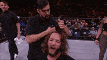 a man is cutting another man 's hair in front of a aew banner