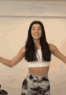 a woman in a white crop top and tie dye skirt is dancing in a room .