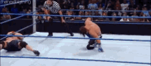 two men are wrestling in a wrestling ring with a referee in the background .