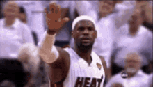 a basketball player wearing a heat jersey is waving his hand in the air .