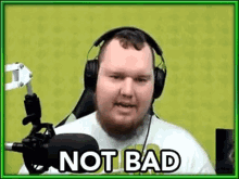 a man wearing headphones and a white shirt is sitting in front of a microphone and says `` not bad '' .