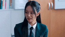 a young woman in a school uniform and tie is sitting in a room .