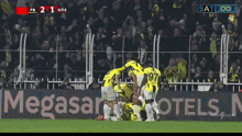 a group of soccer players huddle on a field in front of a megasar hotels sign