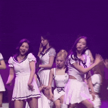a group of girls are dancing on a stage with purple lights