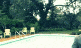a swimming pool surrounded by chairs and trees in a backyard