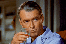 a man in a blue shirt is drinking a glass of wine