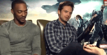 a man in a plaid shirt is sitting next to another man in a grey shirt .