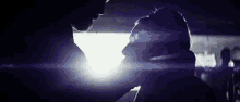 a man and a woman are kissing in a dark room with a light behind them .