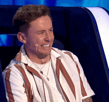 a man wearing a striped shirt is smiling while sitting in a chair