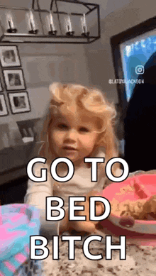 a little girl is sitting at a table with a plate of food and the words `` go to bed bitch '' written on it .