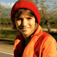 a young boy wearing a red hat and an orange jacket