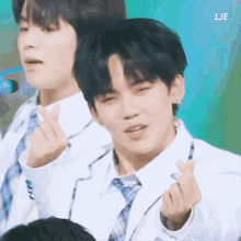 a man in a white suit and tie making a heart with his hands