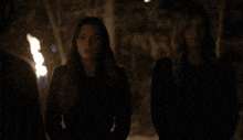two women are standing in a dark room with a fire behind them