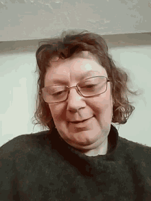 a woman wearing glasses and a black sweater looks down at the camera