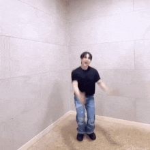 a man in a black shirt and blue jeans is dancing in a room with a white wall .