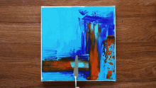 a person is painting a blue and orange painting on a canvas with a knife .