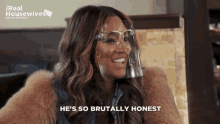 a woman wearing a face shield is smiling and saying he 's so brutally honest