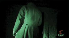 a man in a green coat is standing in a dark room with a travel channel logo in the background