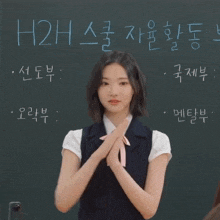 a girl stands in front of a blackboard with foreign writing on it