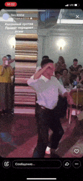 a phone screen shows a man dancing in front of a stack of books and the time is 18:52