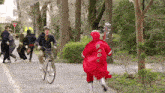 a man on a bike is being followed by a person in a red jacket