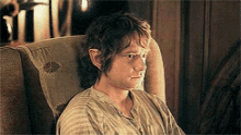a man in a striped shirt is sitting in a chair looking at something .