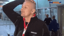 a bald man wearing a sungard jacket holds his hand to his head