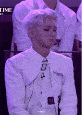 a man with white hair and a white jacket is sitting in a purple room .