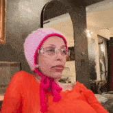 a woman wearing a pink knitted hat and glasses is sitting on a couch .