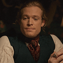 a man with a ring on his finger is wearing a vest and scarf